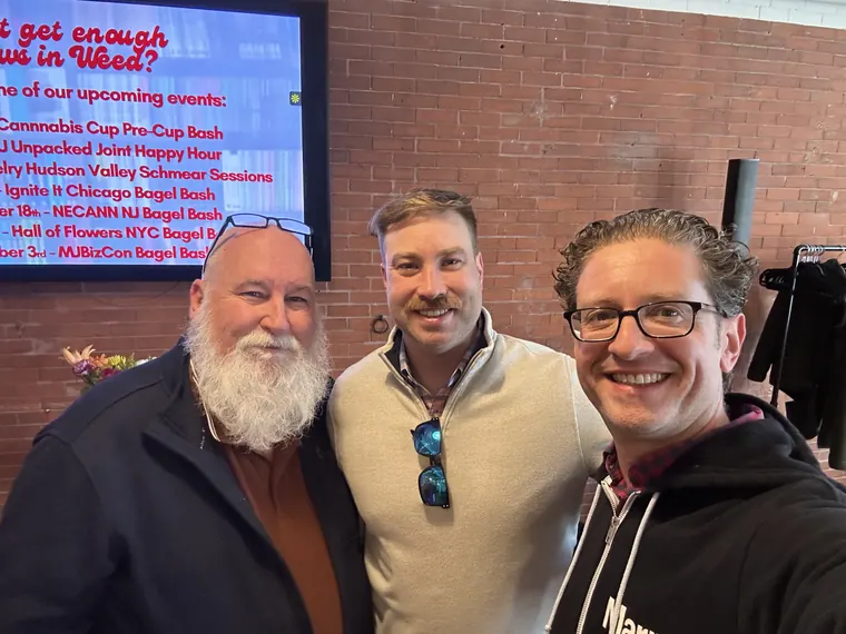 Jordan Isenstadt with two guests in front of the upcoming events screen