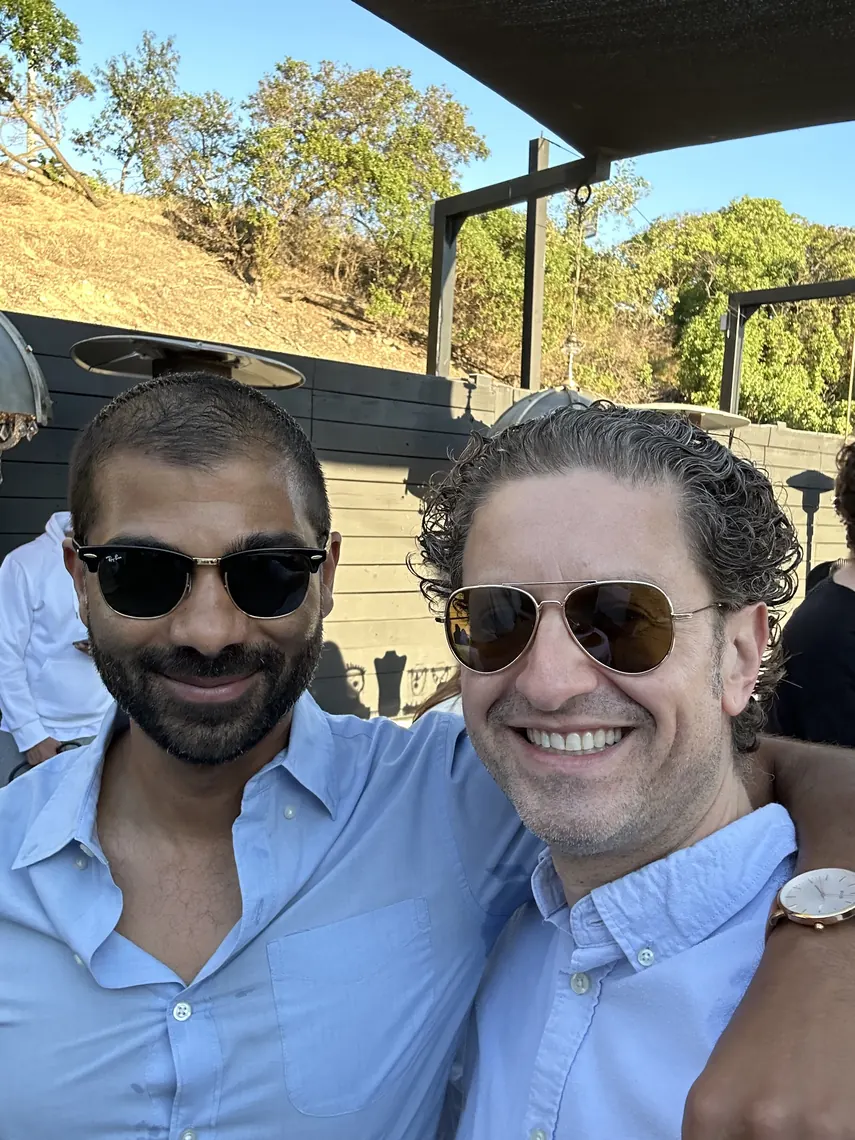 Jordan Isenstadt and a guest in sunglasses smiling on the sunny patio