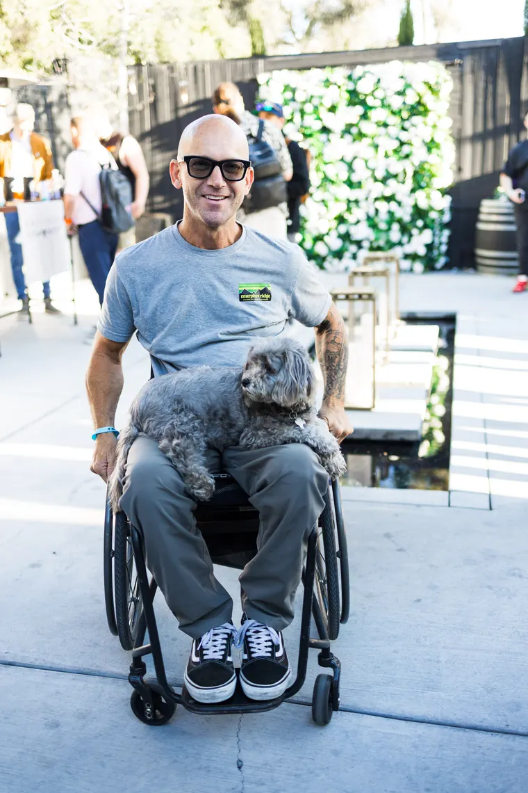 Guest in a wheelchair smiling with a fluffy gray dog on his lap