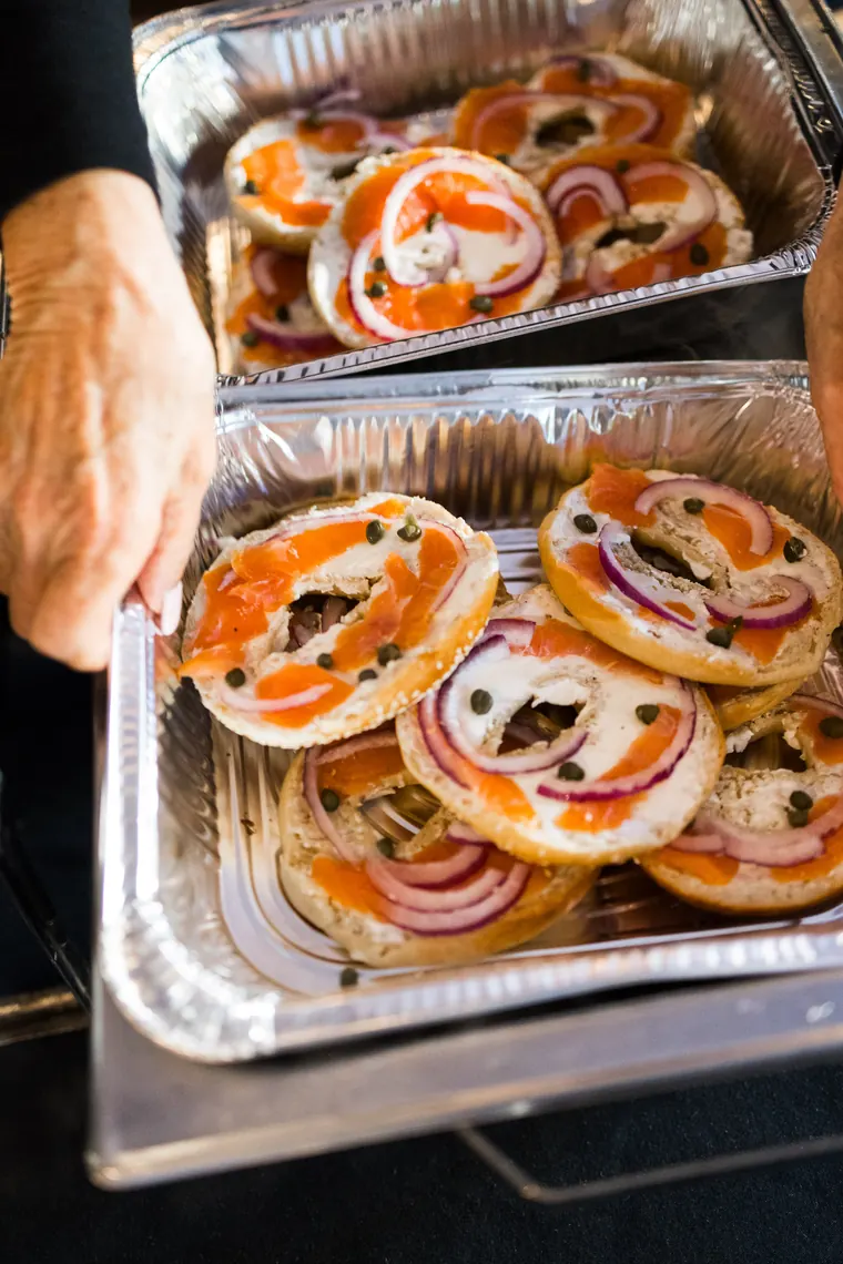 Foil tray of everything bagels topped with lox, cream cheese and red onion