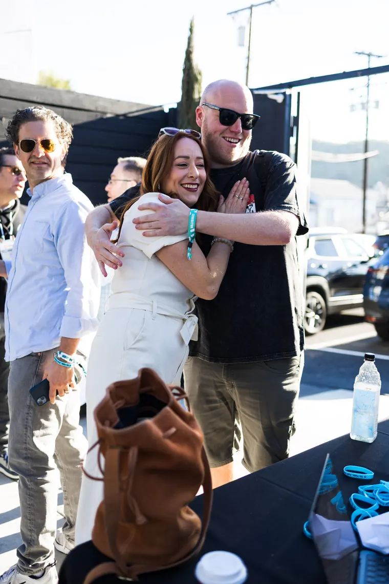 Two guests hugging hello across a table of wristbands