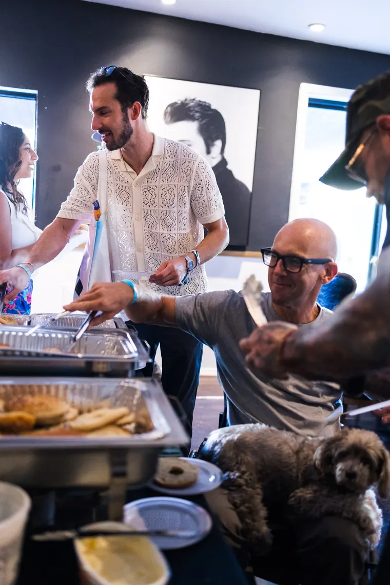 Guests serving themselves at the bagel buffet with a dog waiting below