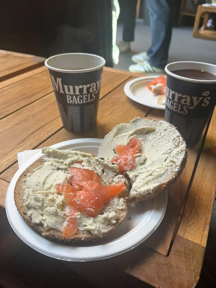 A bagel with cream cheese and lox next to two Murray's Bagels coffee cups