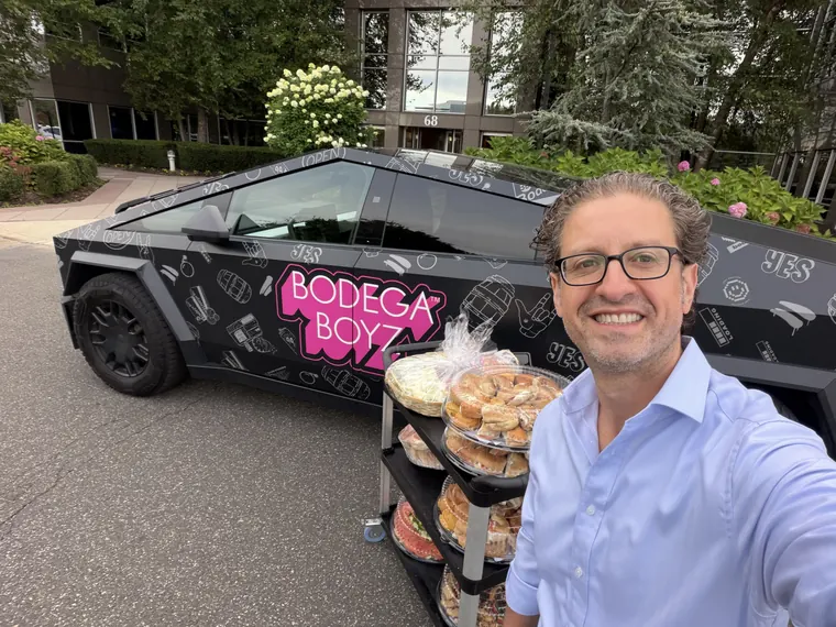 Jordan Isenstadt takes a selfie in front of a Bodega Boyz Cybertruck parked beside a rack of bagel trays outside the RXR Corporate Center