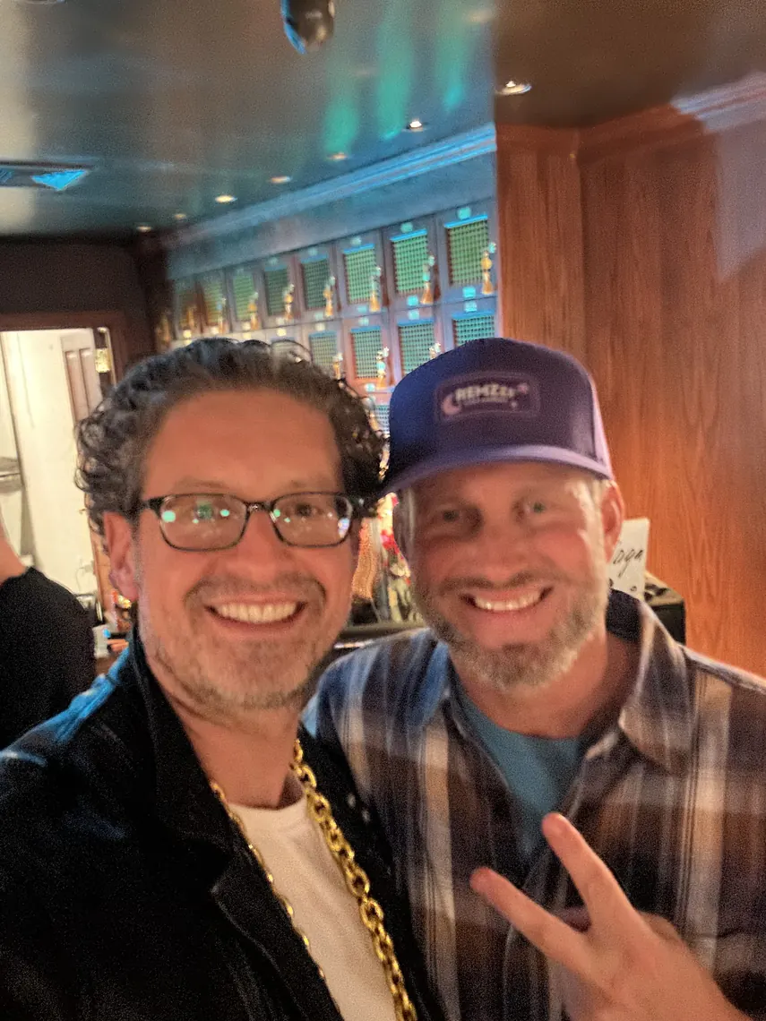 Jordan Isenstadt with a guest in a cap flashing a peace sign